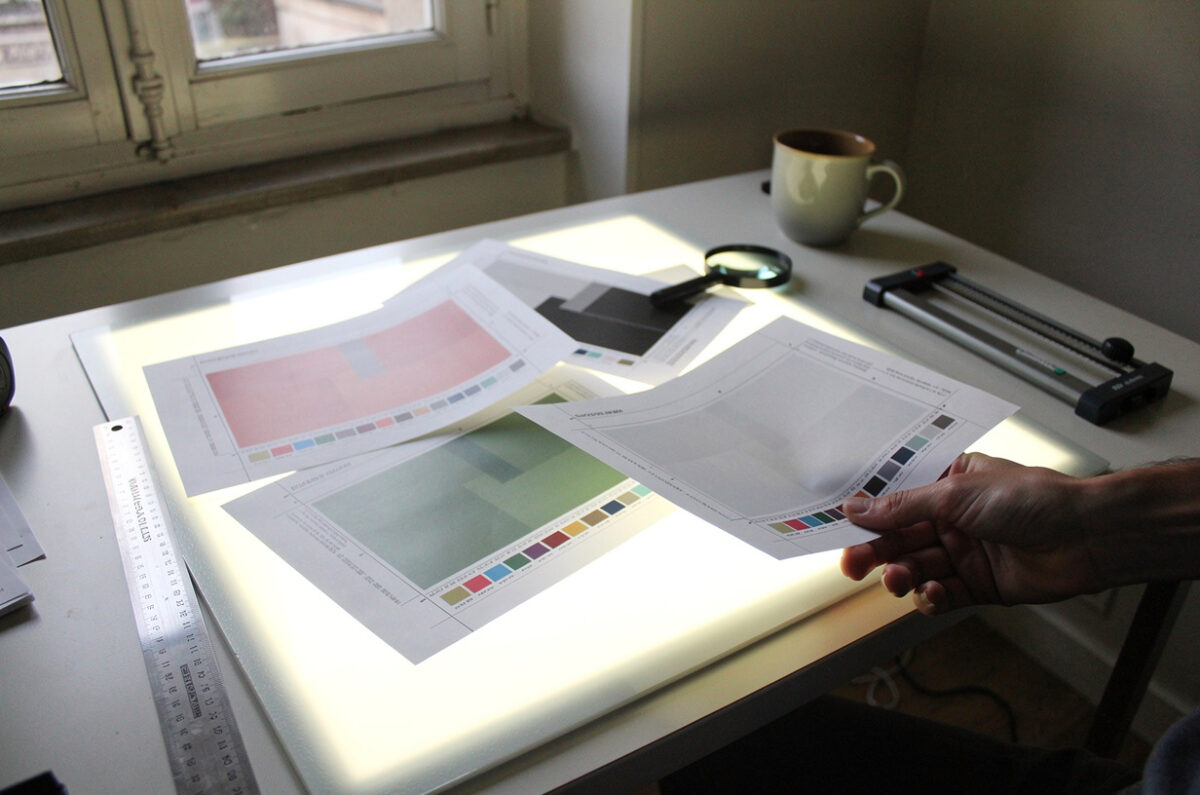 La table lumineuse de l'atelier : des épreuves couleur avec leurs repères de coupe, une règle, une loupe